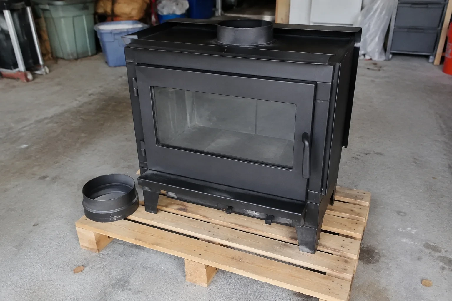 Detached black fireplace insert on a garage pallet.
